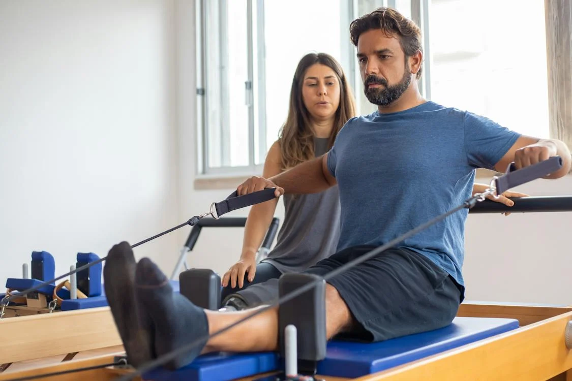 A man sat upright, using elastic to exercise, whilst a physiotherapist behind him oversees the exercise